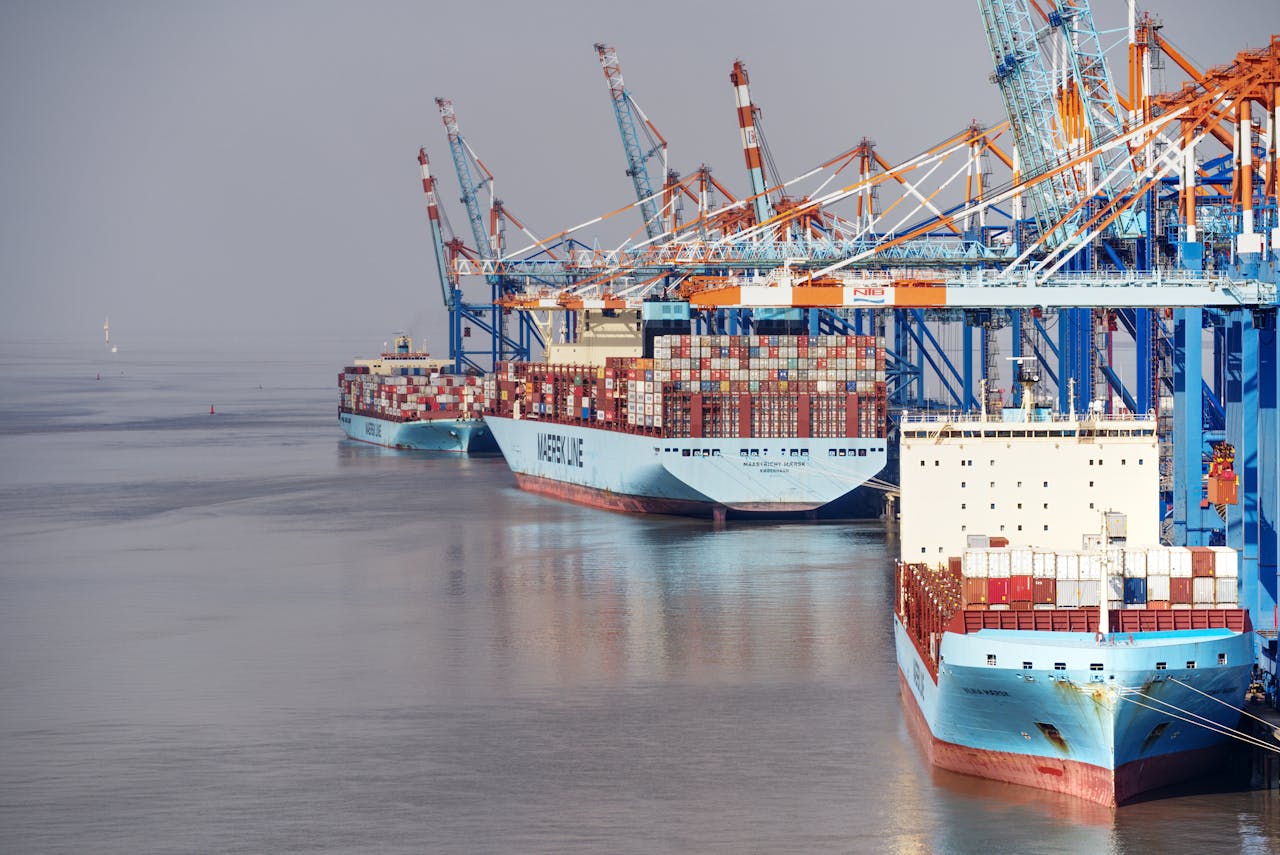 Container ships docked at a busy port with vibrant cranes and clear skies.